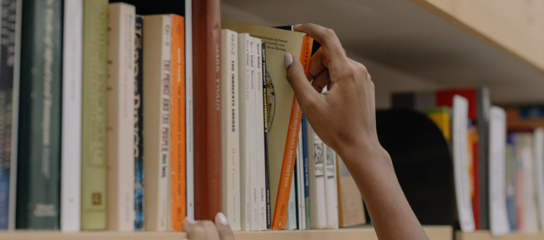 Hand stellt ein Buch in ein Bücherregal