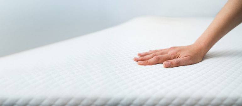 Eine Hand streicht über eine weiße Matratze