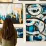 Eine Frau sitzt auf einer Bank vor vielen bunten Bildern an der Wand.