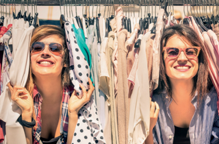 Mädchen mit Sonnenbrillen stehen zwischen aufgehängten T-Shirts