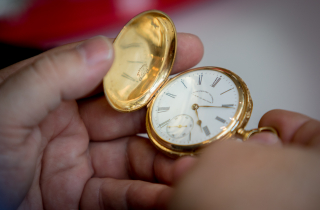 Hände halten eine alte, goldene Taschenuhr in der Hand